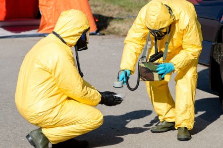 Two people in yellow HAZMAT suits testing an object for radiation