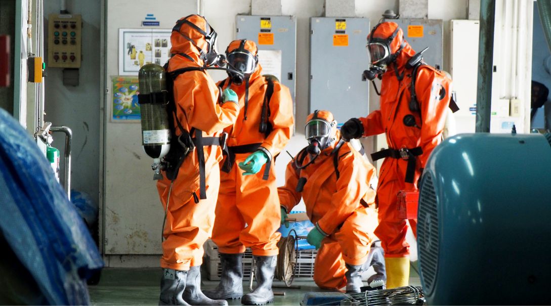 Four people in orange HAZMAT suits discussing who needs HAZWOPER training