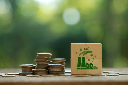 Coins sitting next to wooden blocks with a factory painted on