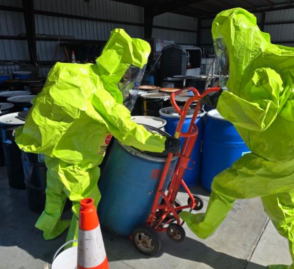 2 people in hazmat suits carrying off toxic barrels