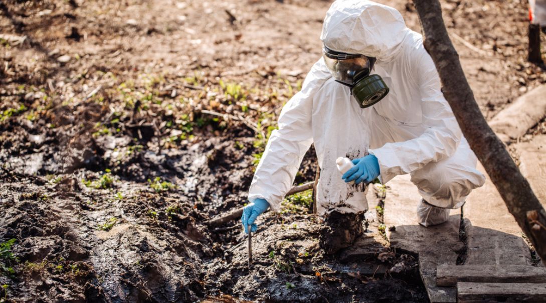 Technician in protective suit collecting soil samples at a contaminated site