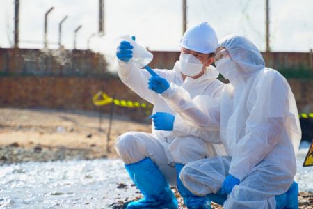 Environmental workers analyzing contaminated water and soil near an industrial spill.