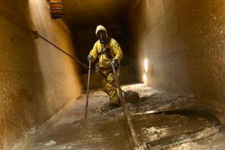 hazmat technician performing confined space industrial cleaning operation.