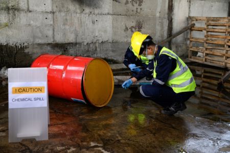 worker assessing a chemical spill beside a leaking industrial barrel
